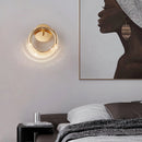 Luxurious metallic wall lamp with an adaptable angle, mounted on a grey wall with wood accents, showcasing circular and rectangular elements.