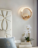 Luxurious metallic rotatable wall lamp with a white light, displayed in an interior setting with houseplants, textiles, and wooden elements.