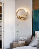 Luxurious metallic rotatable wall lamp with a sleek design, mounted on a wall featuring wood and textile elements in a well-designed interior space.