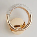 Luxurious metallic wall lamp with a rotatable angle, featuring a sleek design resembling a circular door handle or ring, set on a wooden background.