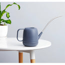 Modern April Showers Garden Watering Can surrounded by houseplants and drinkware on a tabletop, highlighting its functionality and stylish design.
