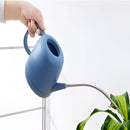 Modern and functional April Showers garden watering can, surrounded by houseplants in an indoor setting, showcasing a stylish, electric blue design.