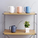 Modern and functional April Showers Garden Watering Can on a table surrounded by houseplants, cups, and dishware under soft lighting.