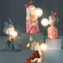 Handcrafted wooden table lamp featuring four artisan-crafted figurines that resemble sisters, designed in a playful and animated cartoon style.