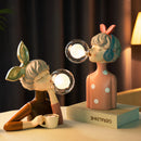 Handcrafted wooden table lamp featuring artistic cartoon-style illustrations and figurative elements, blending traditional craftsmanship with playful design.