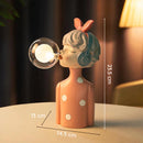 Artisan Sisters Handcrafted Wooden Table Lamp Maisie featuring a unique design with elements resembling a human head, toy-like features, eyewear, and plant accents, crafted from wood and metal.
