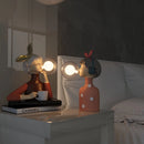 Handcrafted wooden table lamp featuring a unique design with artistic elements and figurine accents in a room setting.