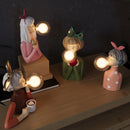 Handcrafted wooden table lamp featuring artistic design elements, displayed among plants and decorative items on a wooden table.