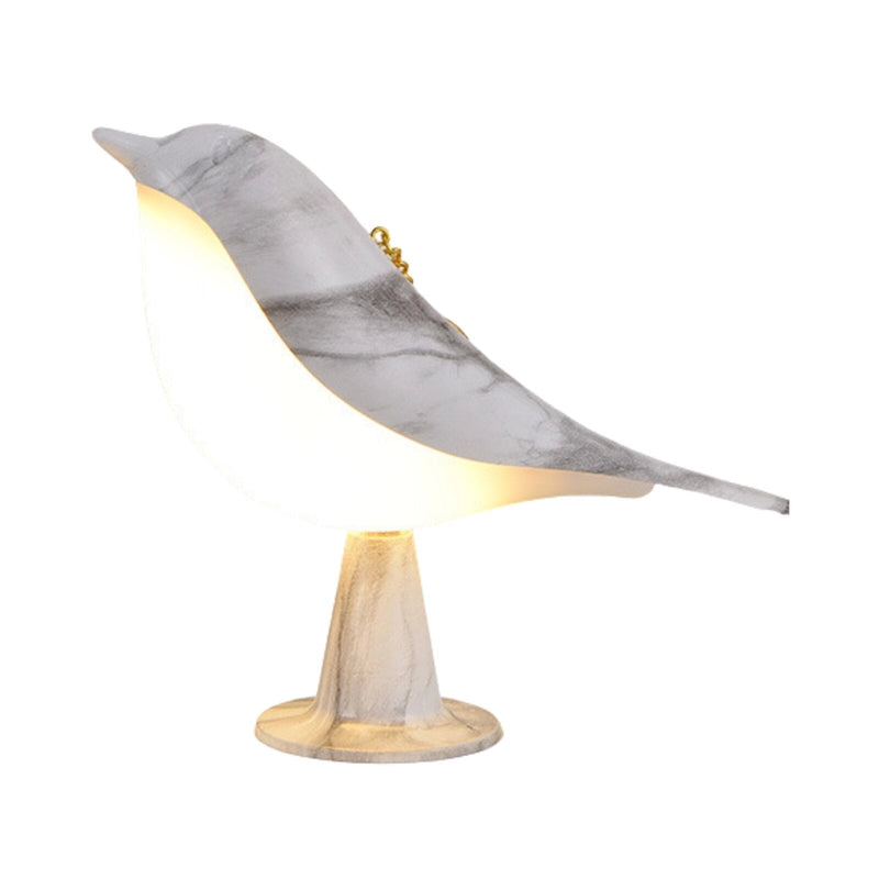 Dimmable LED bird-shaped lamp on a marble base, styled on a wooden chair, combining elements of metal and natural materials in an artistic display.
