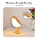 Cordless dimmable LED table nightstand light designed to look like a bird, surrounded by houseplants and wooden decor elements.