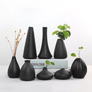 Black ceramic vase for home and garden displayed in a creative still life setting, featuring artistic elements and wood background.