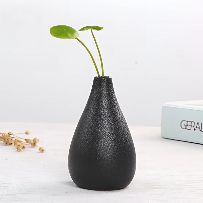 Black ceramic vase designed for home and garden settings, featuring a sleek design and accompanied by twigs and a terrestrial plant, displayed on a wooden surface.