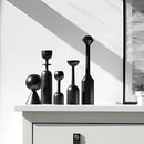 Black wooden candle holder set displayed on shelving, featuring cylindrical and circular shapes, ideal for home decor.