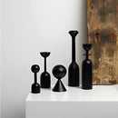 Black wooden candle holder set displayed on a table, featuring cylindrical shapes and crafted from wood and glass, ideal for home decor.