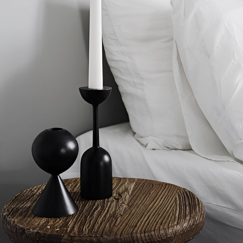 Black wooden candle holder set displayed on hardwood flooring in a monochrome room setting, featuring rectangular shapes and a subtle grey tone.