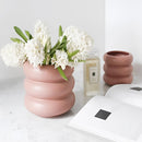 White ceramic bubble glass planter vase on a table, containing a houseplant with visible petals.