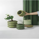 Round ceramic bubble glass planter vase holding a houseplant, placed on a wooden shelf with other dishware and tableware in an interior design setting.