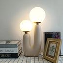 Cactus design table lamp featuring milk glass globes and LED lights, displayed on a wooden floor with artistic interior elements including picture frames and unique ceiling design.