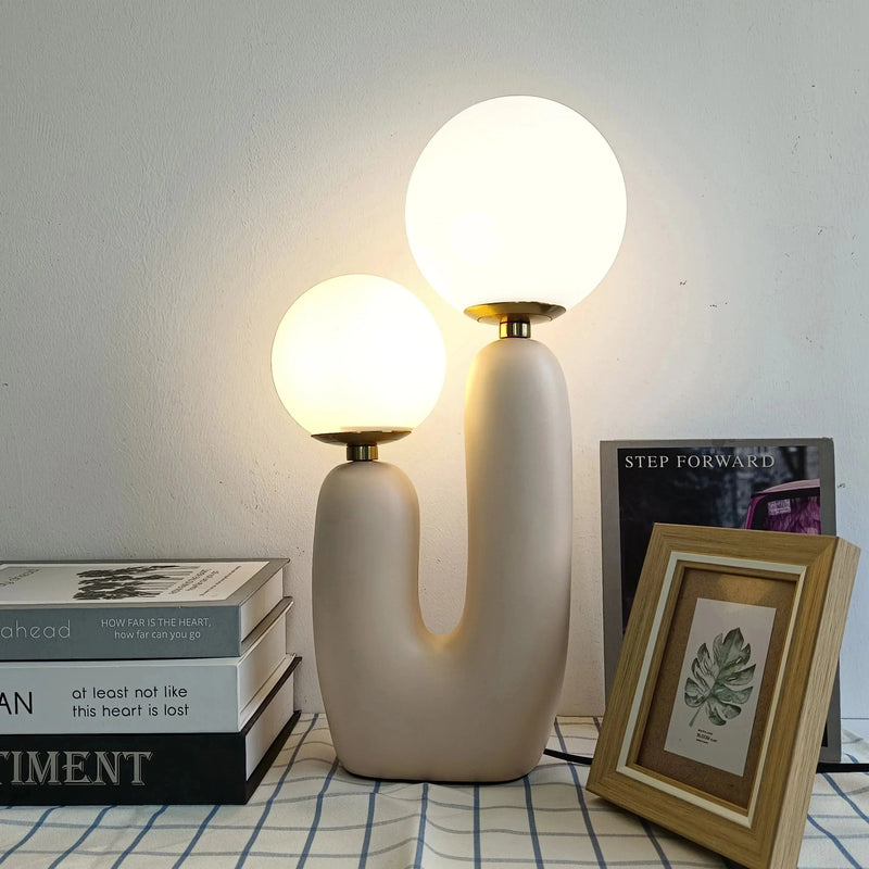 Cactus design table lamp featuring milk glass globes and LED lights, displayed on a wooden floor with artistic interior elements including picture frames and unique ceiling design.