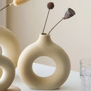 Ceramic donut-shaped vase displayed in a modern home setting with a twig, enhanced by ambient lighting that creates artistic shadows.