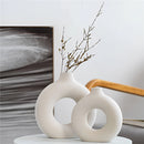A ceramic donut-shaped vase displayed with twigs on a wooden surface, showcasing a modern and artistic design ideal for home decor.