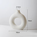 White medium-sized ceramic donut-shaped vase displayed as a piece of modern home decor, featuring artistic and circular design elements.