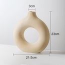 Beige ceramic donut-shaped vase on a wooden surface, designed for modern home decor.