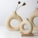 Ceramic donut-shaped vase featuring a modern design, displayed with twigs on a wooden surface, enhancing a contemporary home decor aesthetic.