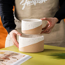 White and yellow ceramic flowerpot held in a hand, displayed on a table.