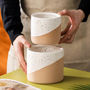 Hand holding a small ceramic flowerpot in linen texture, placed on a wooden surface.