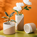 Ceramic flowerpot in linen color containing a vibrant yellow flowering plant with lush green leaves, suitable for indoor use.