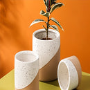 Ceramic flowerpot in linen color featuring a small, medium, and large size, displayed with a houseplant, on a table setting among various dishware and drinkware items made of porcelain and pottery.