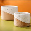 Assorted small, medium, and large ceramic flowerpots in linen color, displayed on a table, showcasing cylindrical shapes and a smooth porcelain finish.