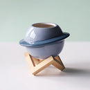 Ceramic plant pot with an astral galaxy design, resembling a decorative hat, placed on a wooden surface.