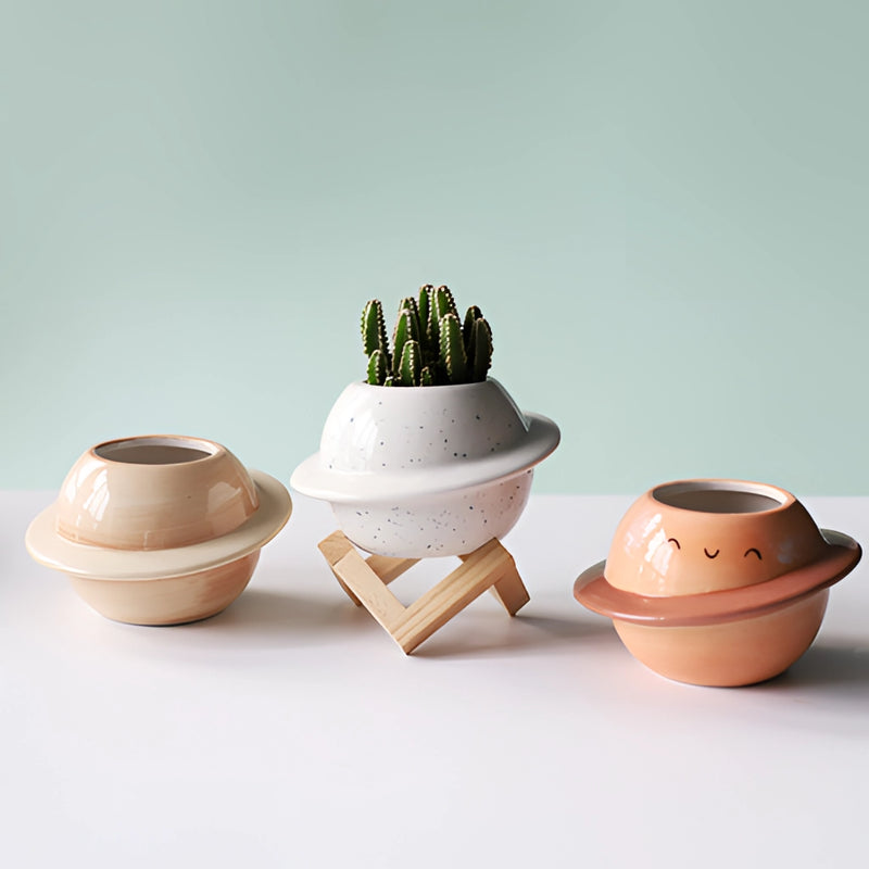 Ceramic planet-shaped plant pot with an astral galaxy design, featuring porcelain and earthenware textures on a wooden surface.