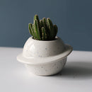 White Ceramic Planet Plant Pot with Astral Galaxy Design, featuring a houseplant and decorative tableware elements on display.