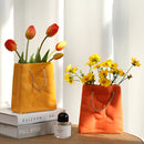 Ceramic vase with a shopping basket design, featuring orange and yellow flowers, including petals and plants, arranged inside, enhancing the interior design with subtle lighting.