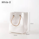 Small white ceramic vase designed to resemble a shopping basket, featuring intricate details that mimic metal chain jewelry.