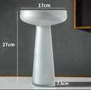 Coffee-colored frosted glass vase on a table, displaying a transparent appearance with subtle artistic elements and lighting accessories surrounding it.