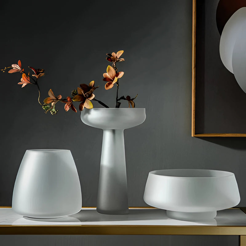 Coffee-colored frosted glass vase on a table, surrounded by houseplants and dishware, in a well-lit interior setting.
