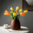 Coffee-colored frosted glass vase on a table, featuring a delicate arrangement of orange flowers with visible petals, complemented by interior design elements including a coffee cup.
