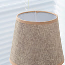 Beige fabric lampshade on a wooden desk with a chair in the background, enhancing a contemporary home setting.