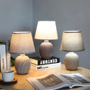 Rechargeable table lamp with a unique contemporary style, featuring a wooden base and a textile shade, displayed in an interior setting with books and artistic decor elements.