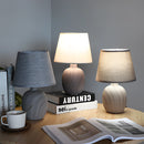 Contemporary rechargeable table lamp with unique style, featuring a grey textile lampshade on a wooden base, placed next to a book on a grey floor.