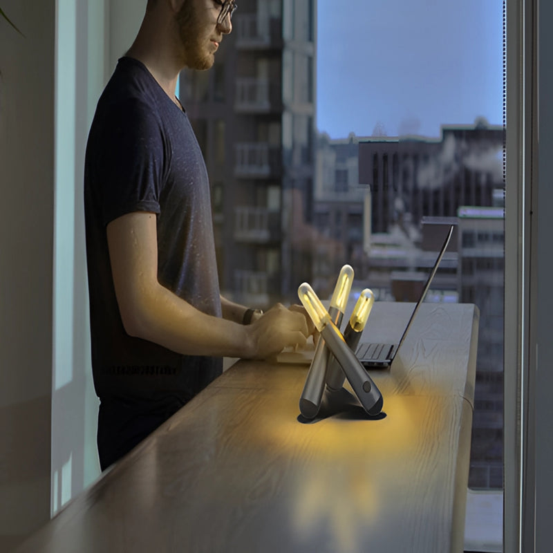 A white-collar worker demonstrating the features of a Cordless Kinetic Rotation LED Table Lamp, wearing a T-shirt and eyewear, with a clear sky in the background.