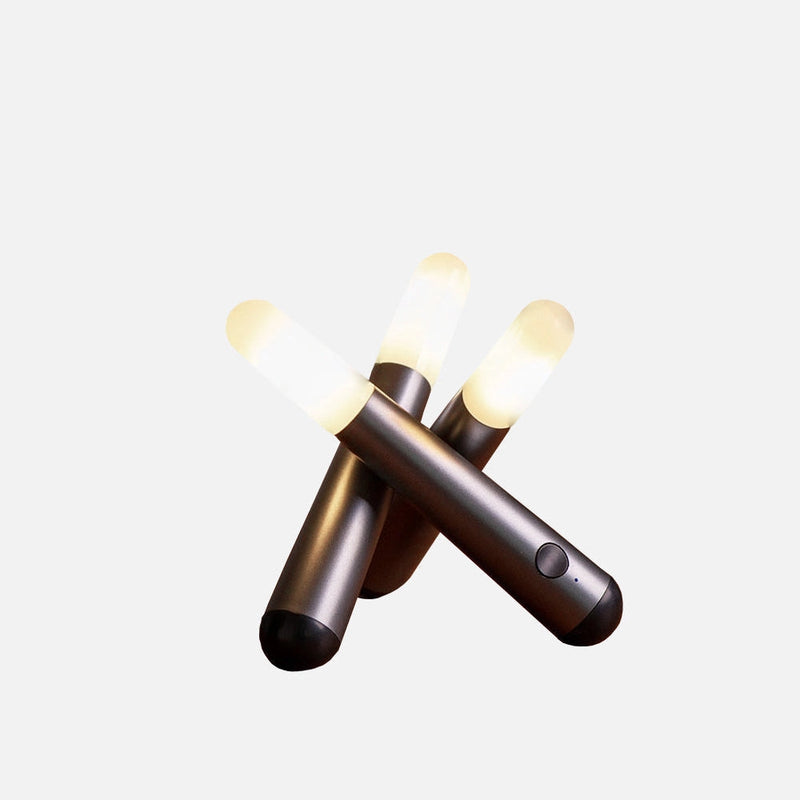 Cordless kinetic rotation LED table lamp on a beige wooden surface with metal and plastic components illuminated below a ceiling.