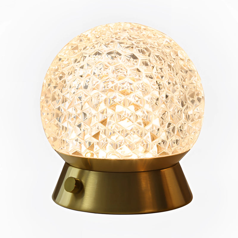 Modern cordless rechargeable LED table lamp with dimmable light, featuring a lampshade, set on a wooden surface near plants and metallic elements.