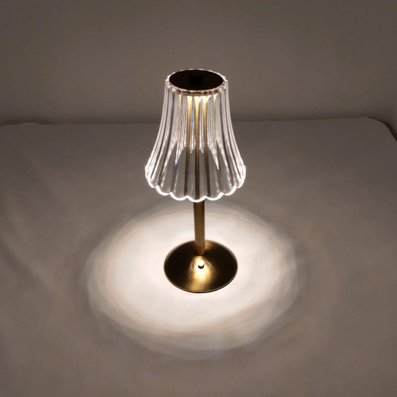 Cordless table lamp with a metal base and circular wooden lampshade displayed on a wooden table.