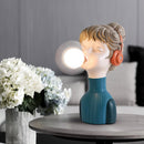 Orange and green desk lamp designed to resemble a flowering plant with artificial petals, providing a chic minimalist look.