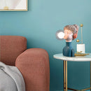 Chic minimalist design desk lamp in orange and green, featuring a sleek line and azure accents, positioned on a table against a blue wall in a stylish interior setting.